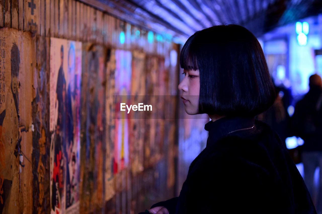 Close-up of woman looking at old posters on wall in illuminated city