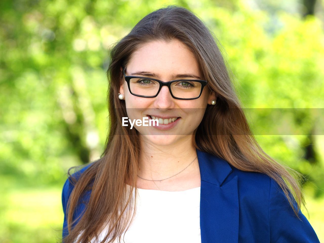 Close-up portrait of young woman smiling while standing against trees