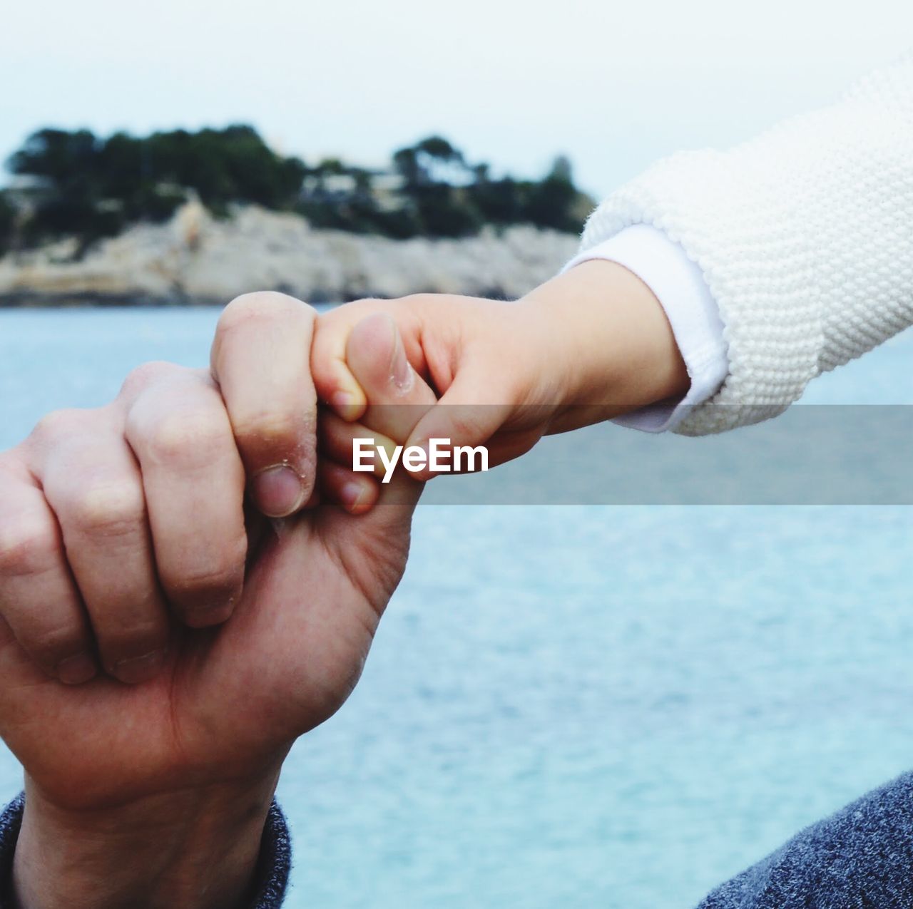 Close-up of cropped father holding daughter hand against sea