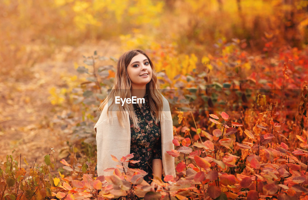 PORTRAIT OF A SMILING YOUNG WOMAN IN AUTUMN LEAVES