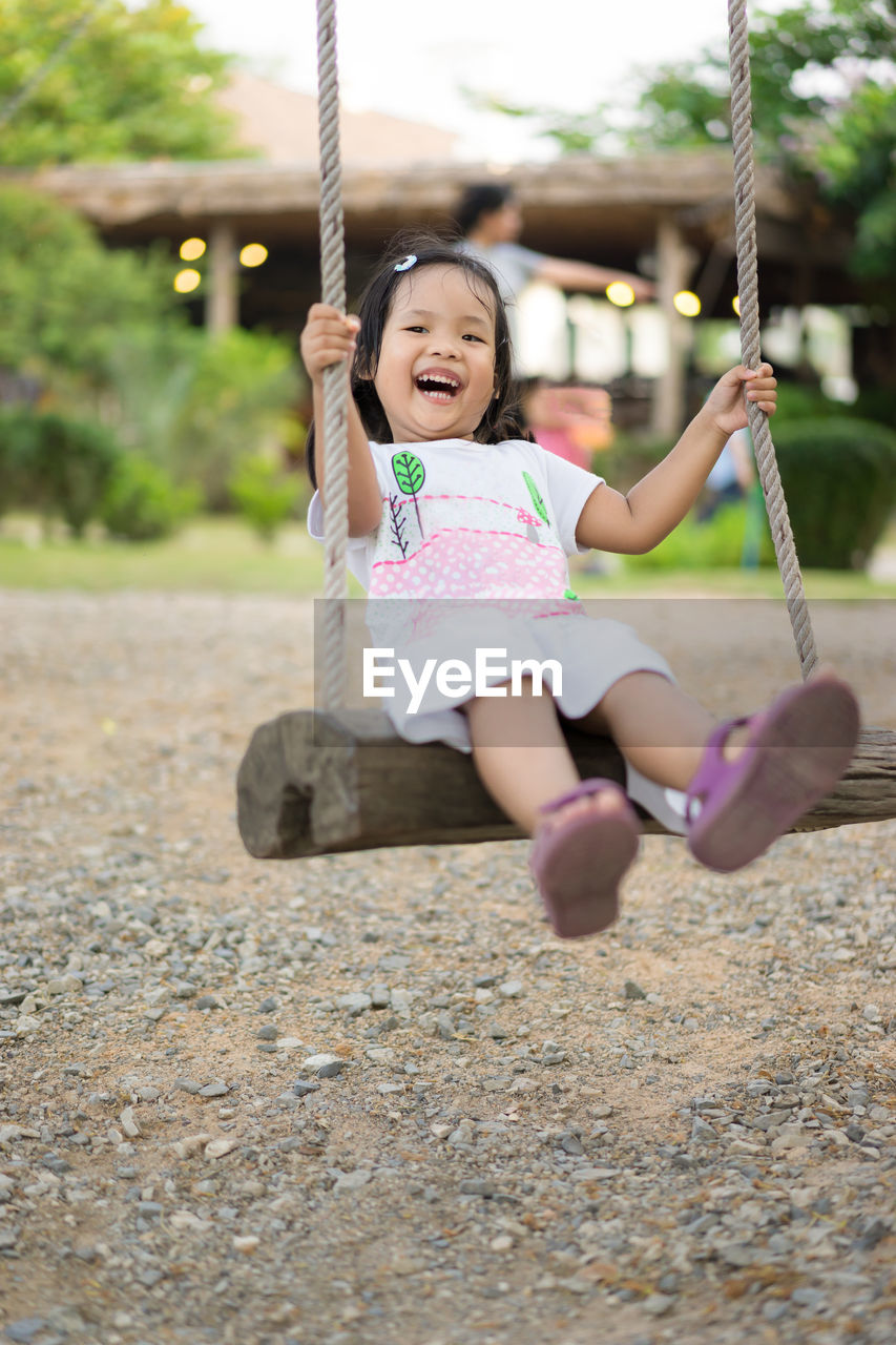 Portrait of smiling girl sitting on swing at playground