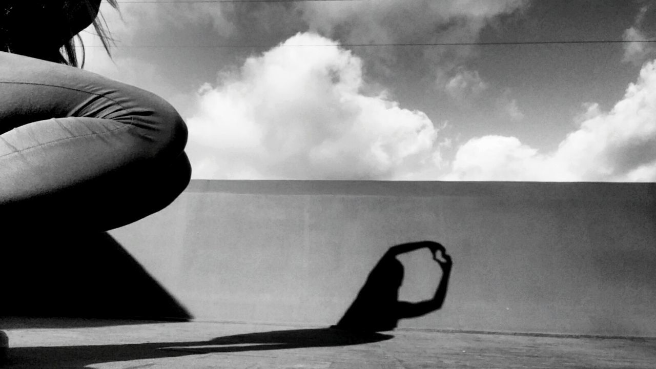 Midsection of woman with heart shadow on retaining wall against sky