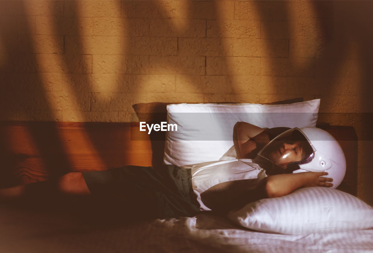 Girl wearing helmet while lying on bed at home