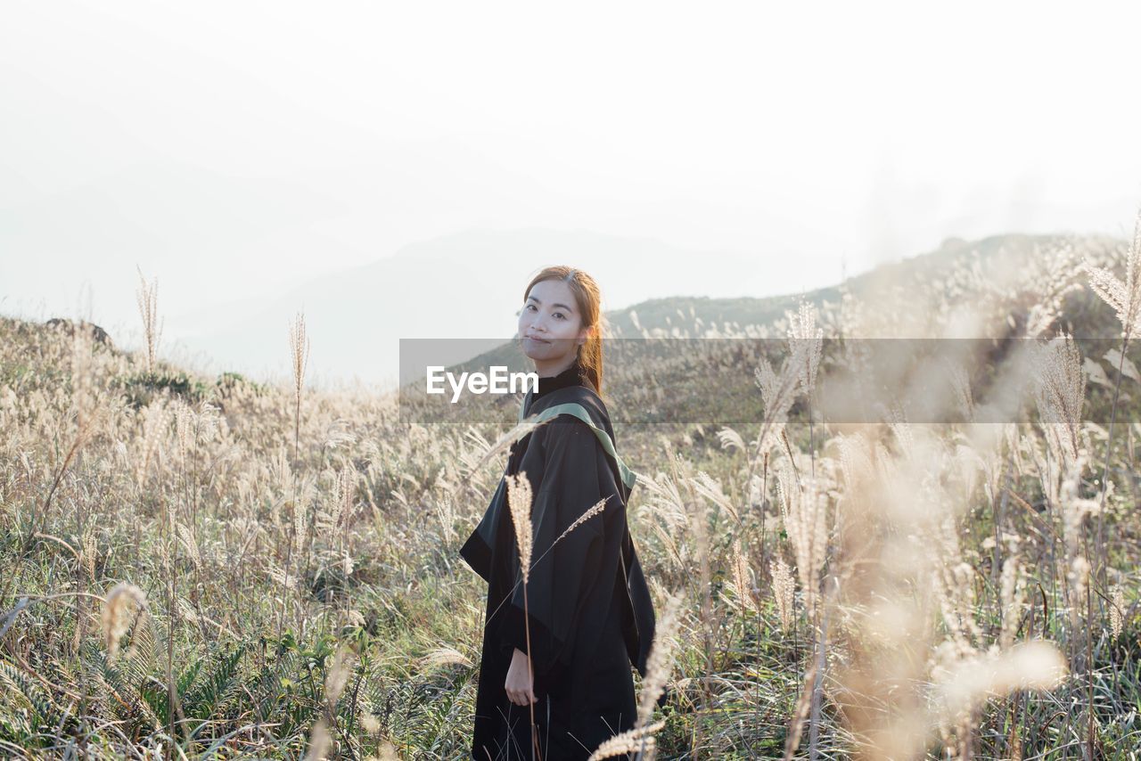 Portrait of smiling young woman standing on grassy field against clear sky