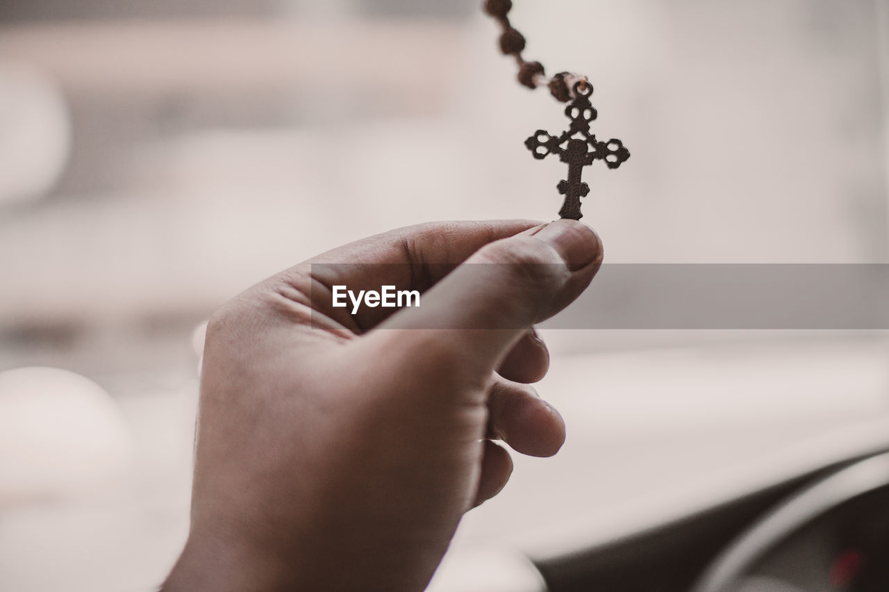 Close-up of hand holding rosary beads against blurred background