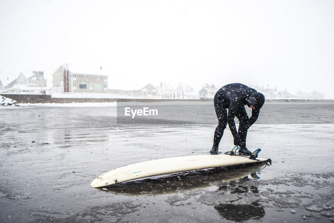 Surfer checking the bottom of board during a maine snow storm