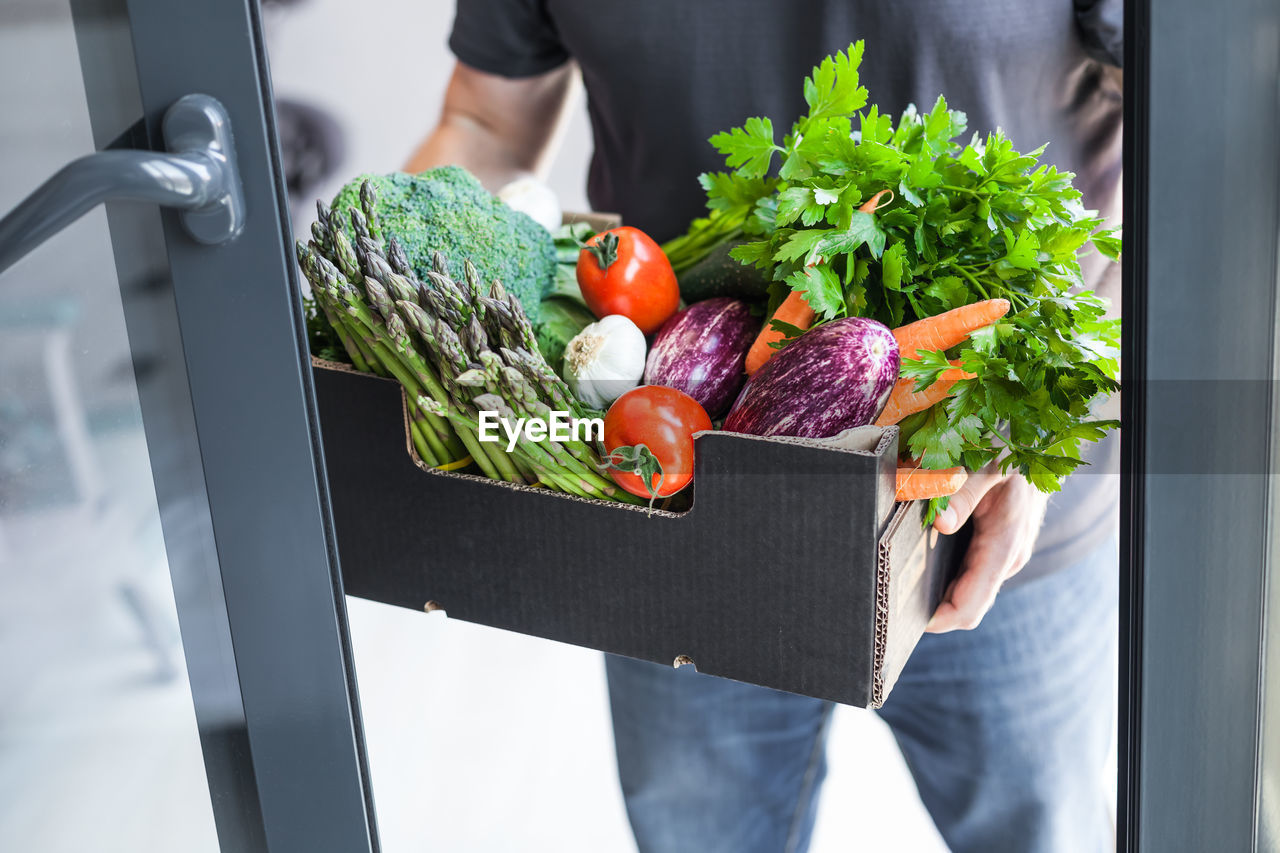 MIDSECTION OF MAN HOLDING VEGETABLES IN CONTAINER