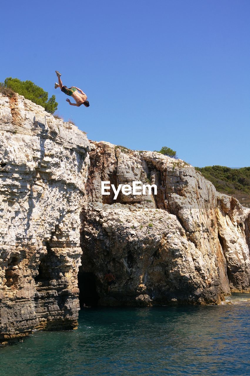 Person jumping in sea against clear sky