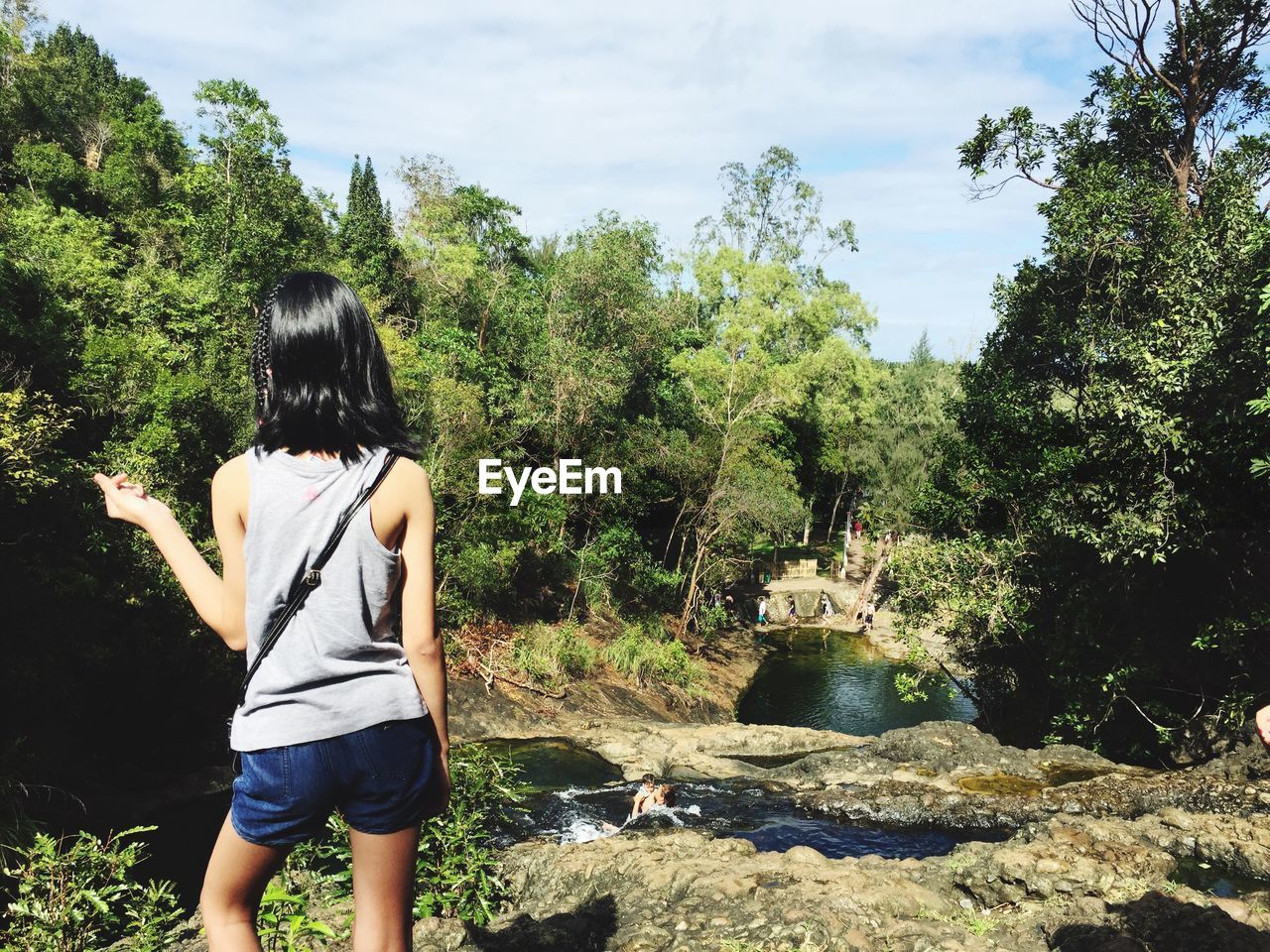 REAR VIEW OF PERSON STANDING ON ROCK AGAINST SKY