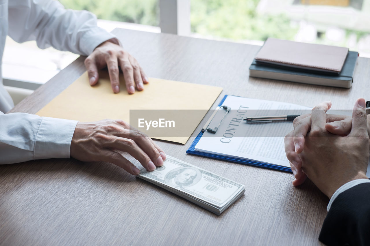 Cropped image of man bribing businessman on table