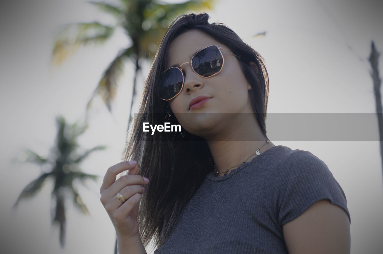 PORTRAIT OF BEAUTIFUL YOUNG WOMAN WEARING SUNGLASSES AGAINST SKY