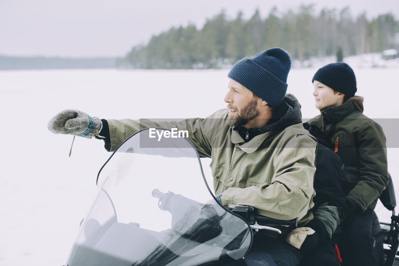 Mature man gesturing while snowmobiling with boys