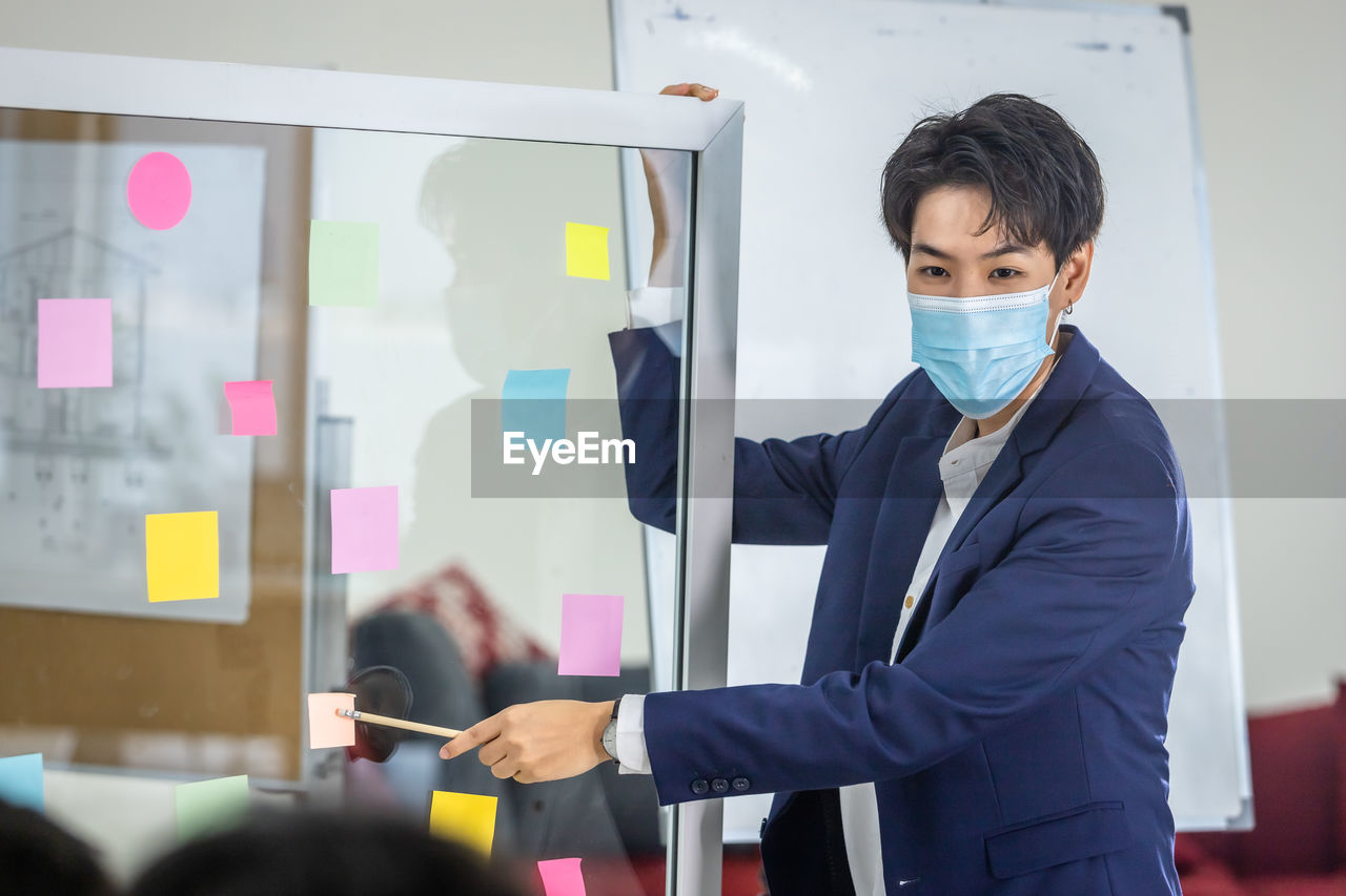 Portrait of young businessman wearing mask giving presentation in office