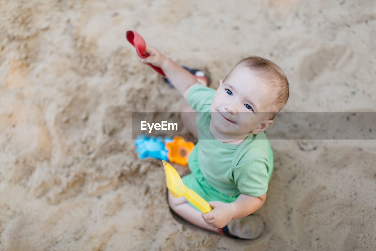 High angle view of cute baby boy looking up while playing on sand at beach