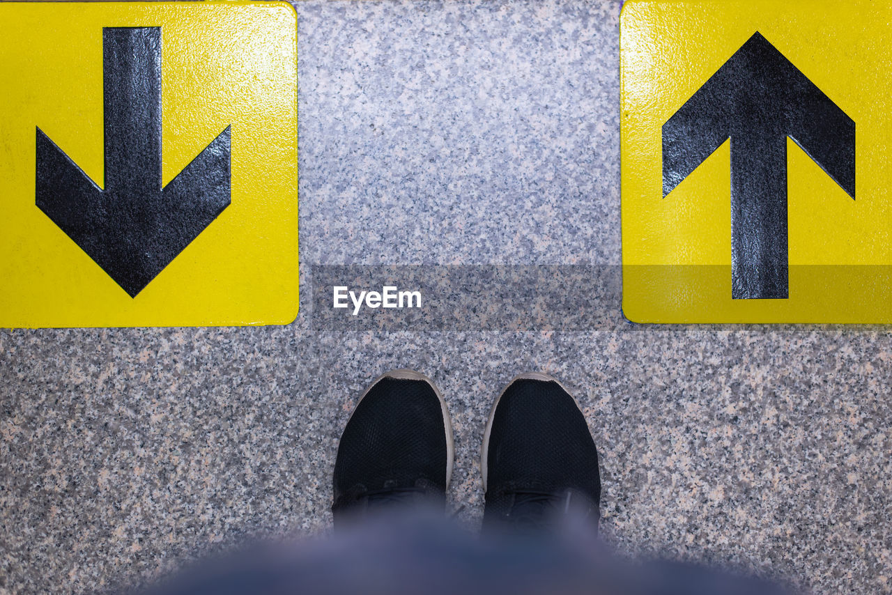 LOW SECTION OF MAN STANDING BY ARROW SIGN