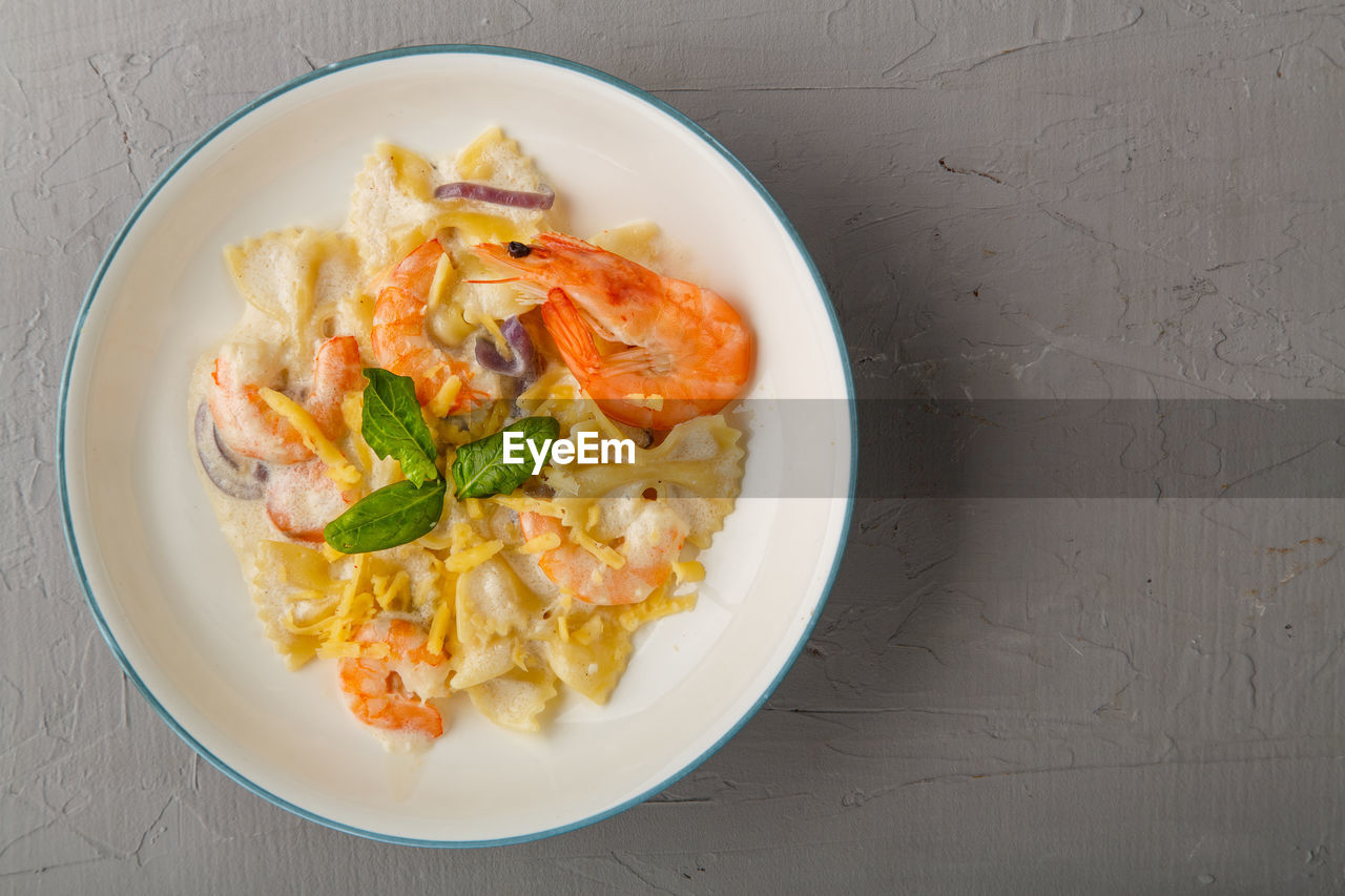 Pasta with shrimps in a creamy sauce on a gray plate on a concrete background. copy space horizontal