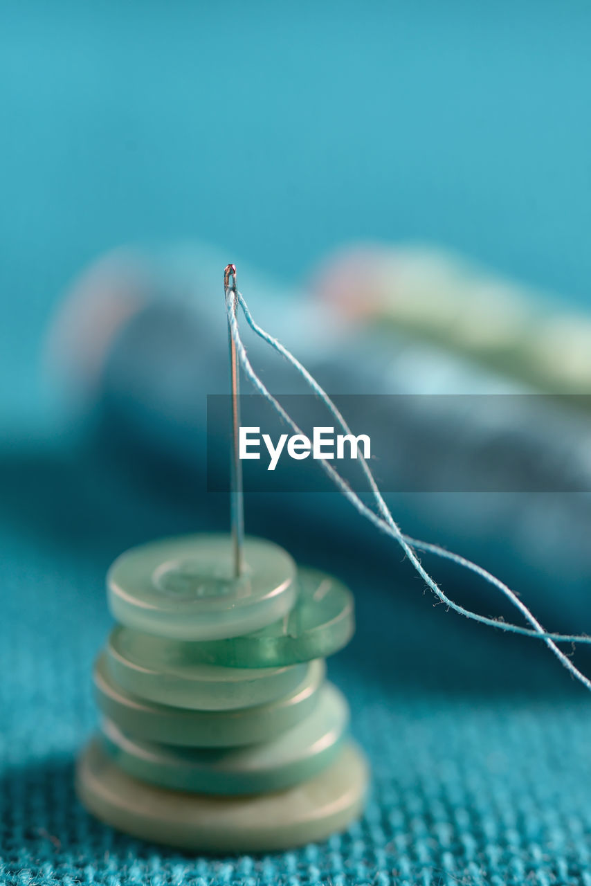 Close-up of sewing needle with button and thread spools on table