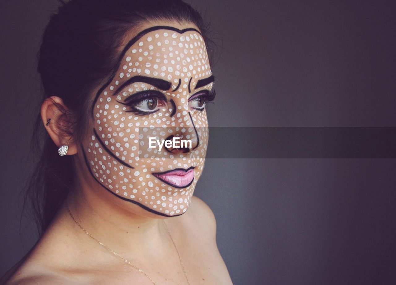 Close-up of young woman with face paint while standing on gray background