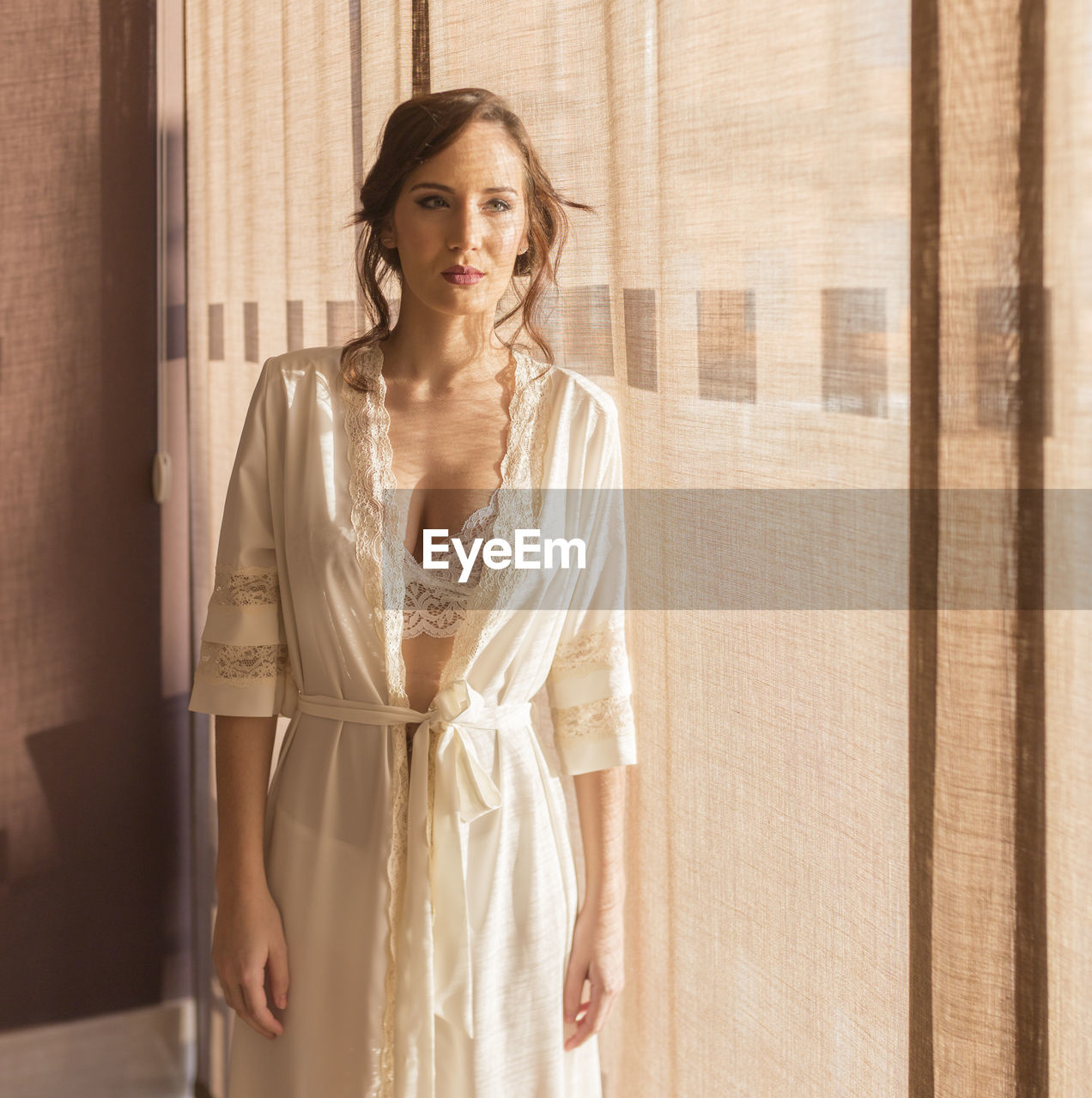 Beautiful young woman standing by curtain at home