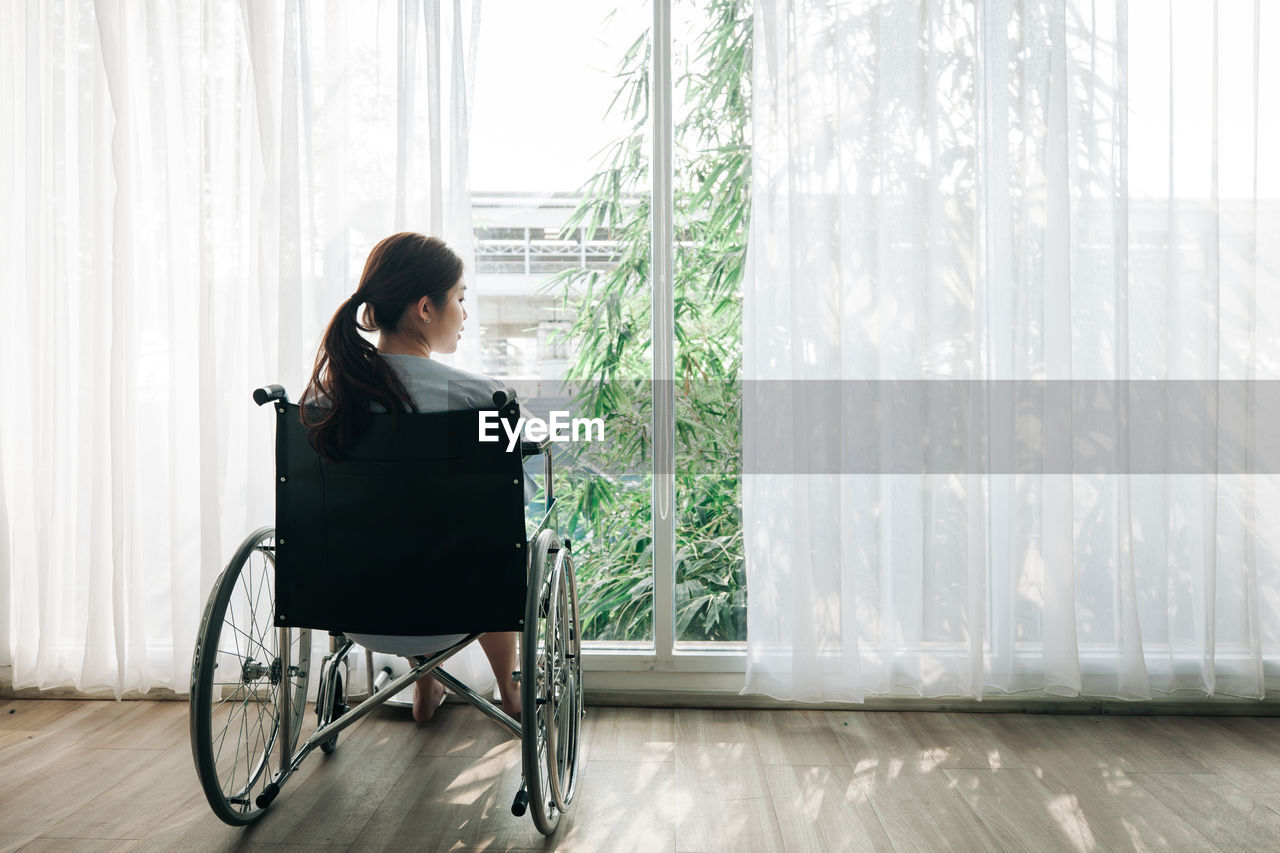 WOMAN SITTING ON WINDOW IN FRONT OF WOODEN WALL