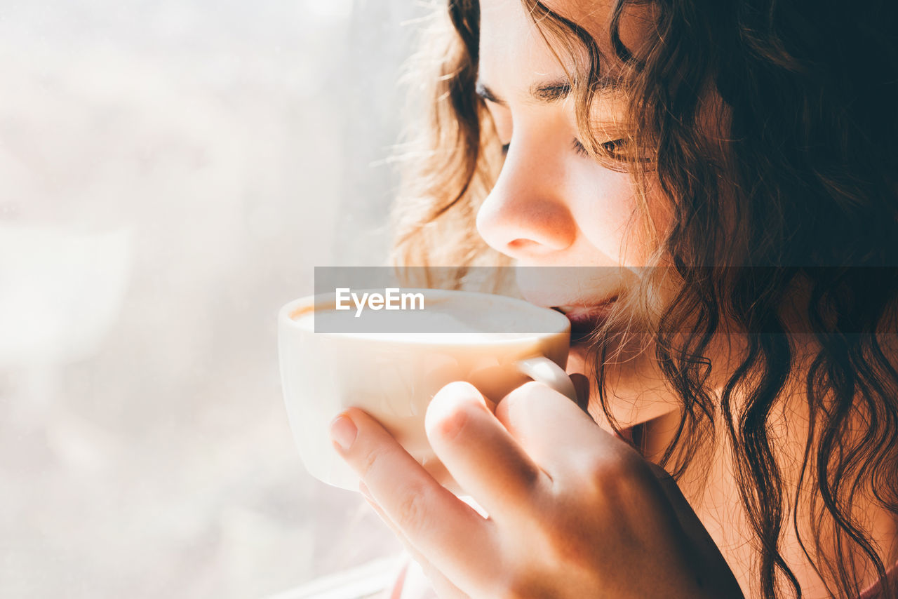 Beautiful woman drinking coffee near the window. close up portrait.