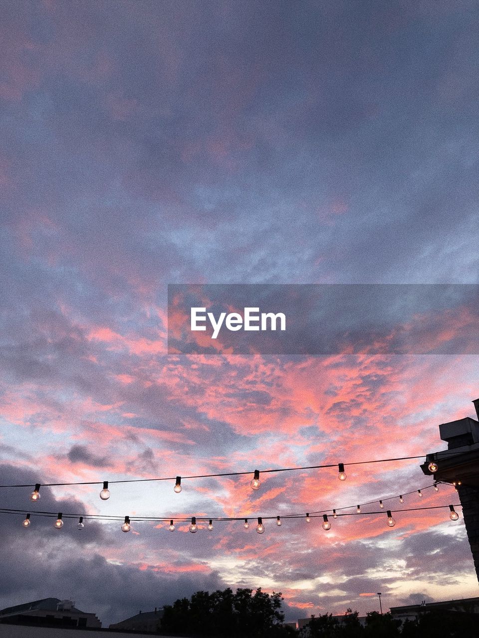 Low angle view of illuminated light bulbs against dramatic sky during sunset