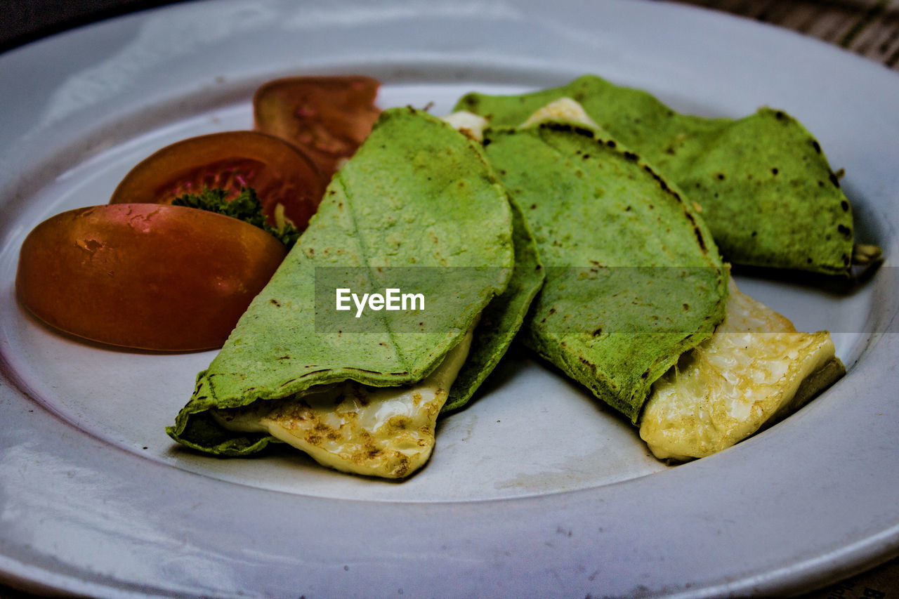 Close-up of delicious quesadillas in white plate on table, green tortilla with panela cheese