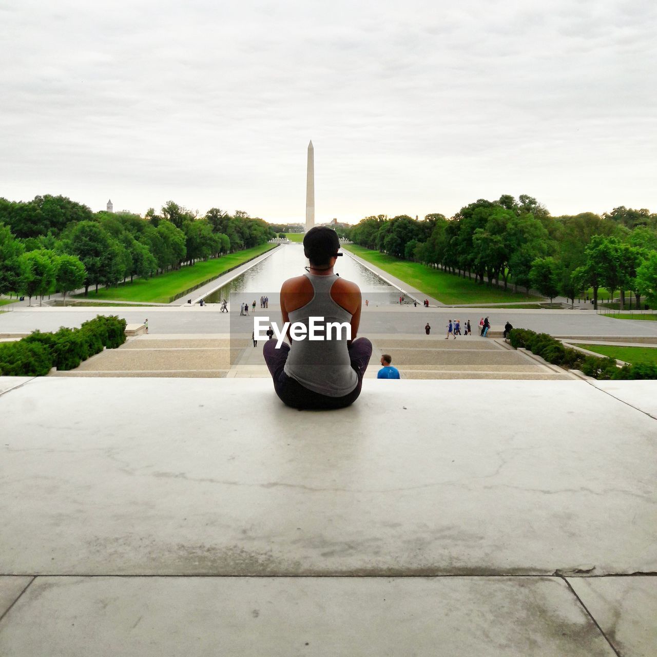 FULL LENGTH REAR VIEW OF WOMAN SITTING ON RIVERBANK AGAINST SKY