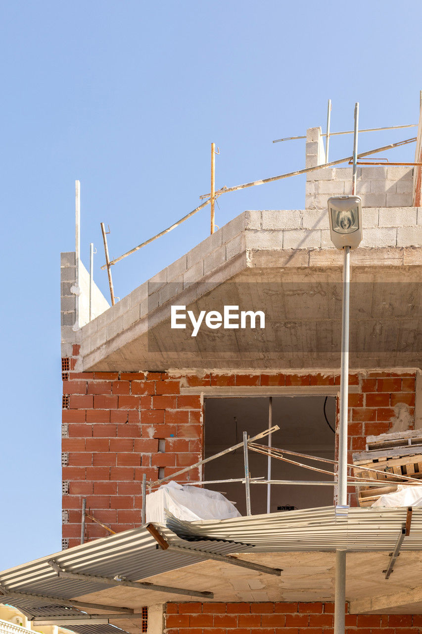 Close-up of an urban construction site with unfinished brick and concrete building under clear skies