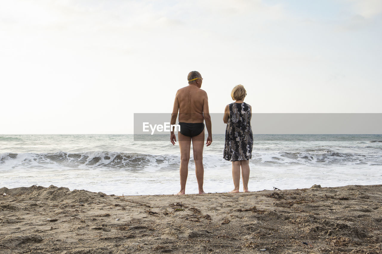 Italy, sicily, senior couple at the beach looking at the sea