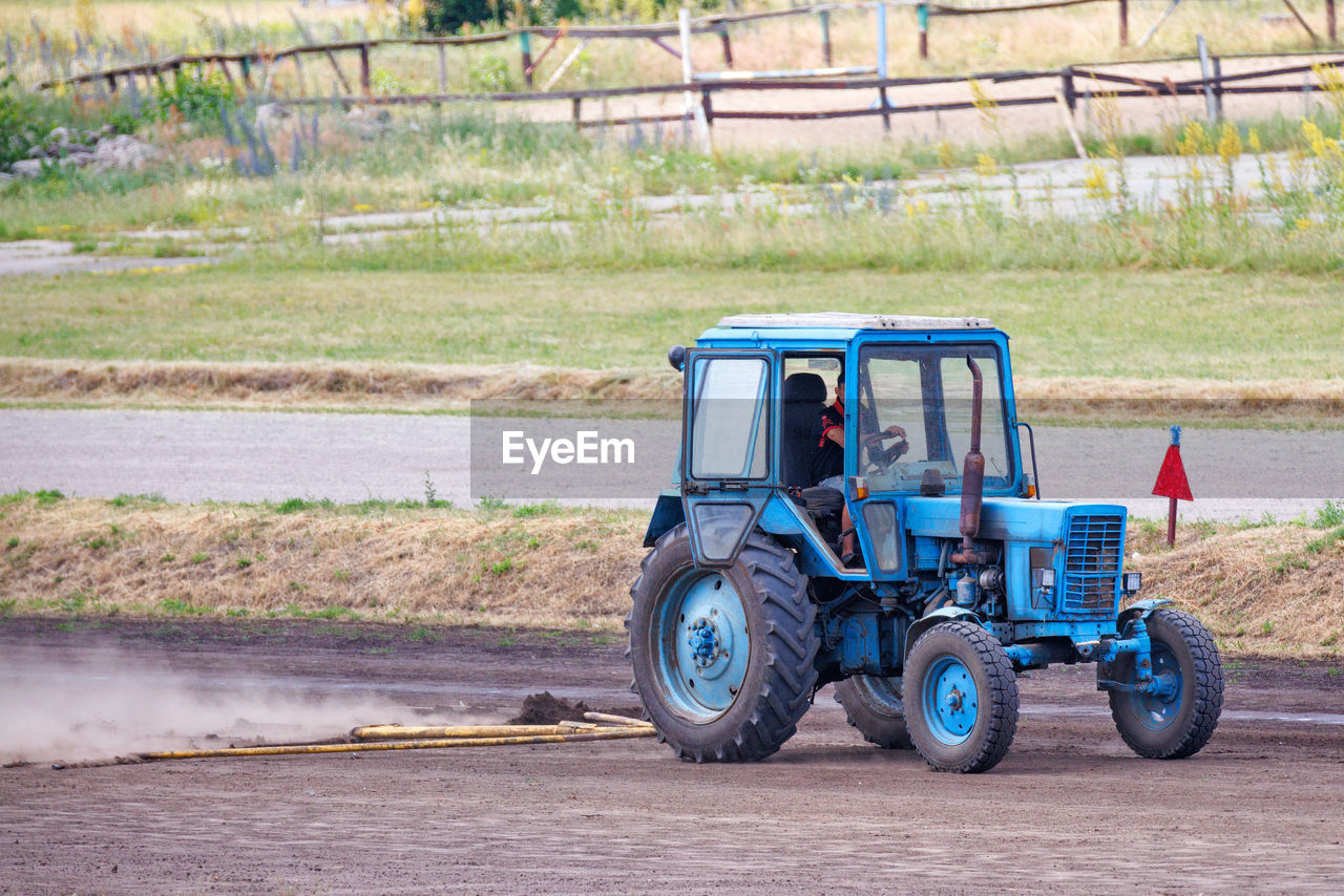 tractor, transportation, mode of transportation, agricultural machinery, land vehicle, vehicle, agriculture, field, road, nature, driving, landscape, day, soil, machinery, land, asphalt, farm, agricultural equipment, rural scene, outdoors, plant, occupation, working, wheel, one person