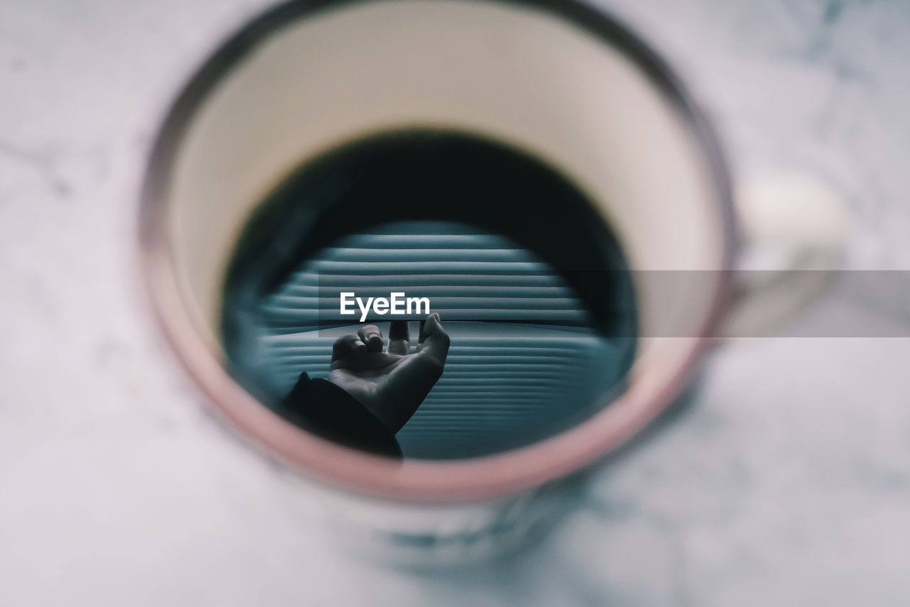 Cropped hand of person reflecting in coffee cup