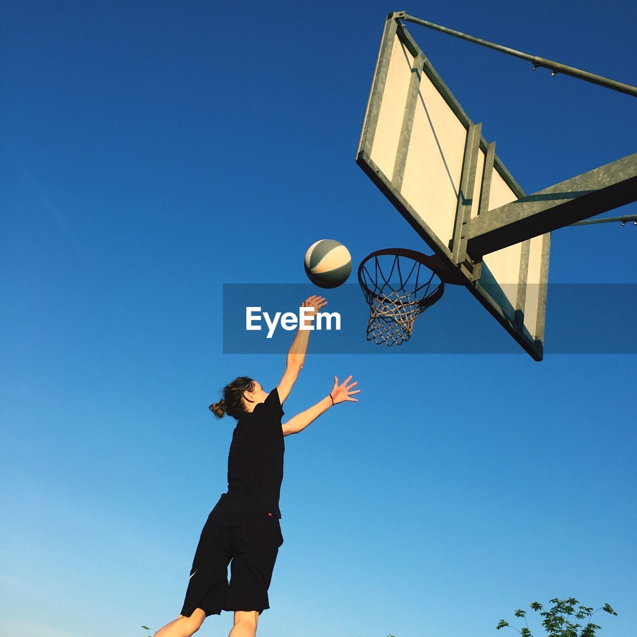 Low angle view of teenage girl playing basketball against clear blue sky
