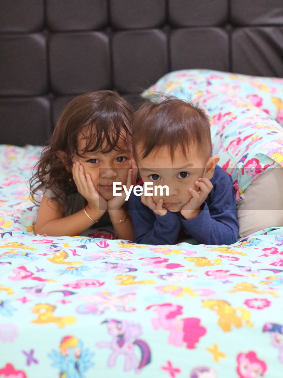 Portrait of cute siblings lying on bed at home