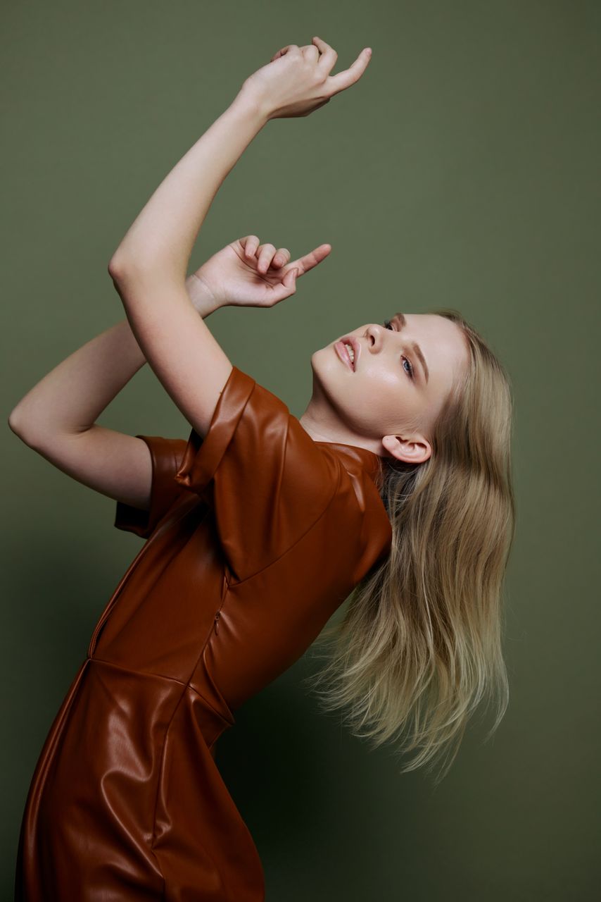 portrait of smiling young woman with arms raised standing against wall