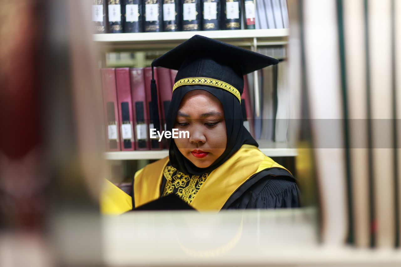 Young woman wearing graduation gown in library