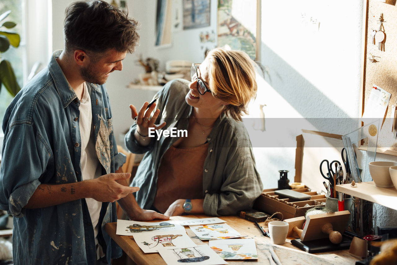 Happy businesswoman discussing over sketches with male colleague at home office