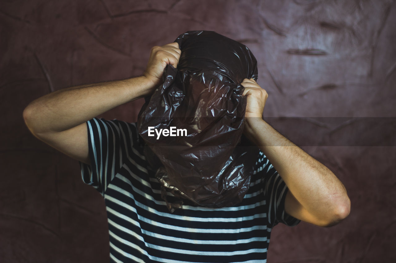 Man with face covered by plastic bag against wall