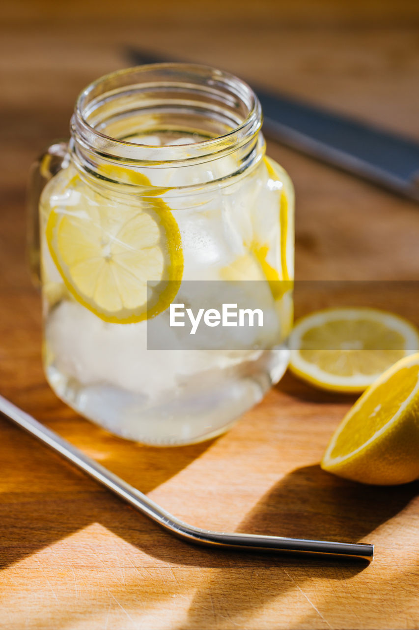 From above metallic reusable straw and glass jug with ice and lemon slices on wooden table in kitchen