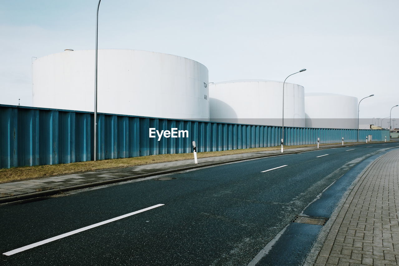 Road by fuel storage tank against sky