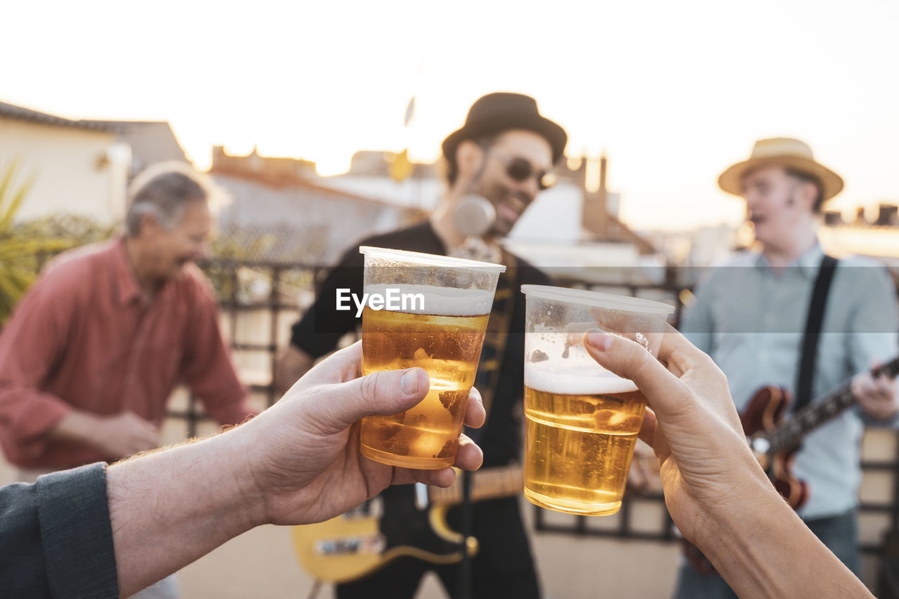 Cropped hand of person holding beer glass against musicians outdoors