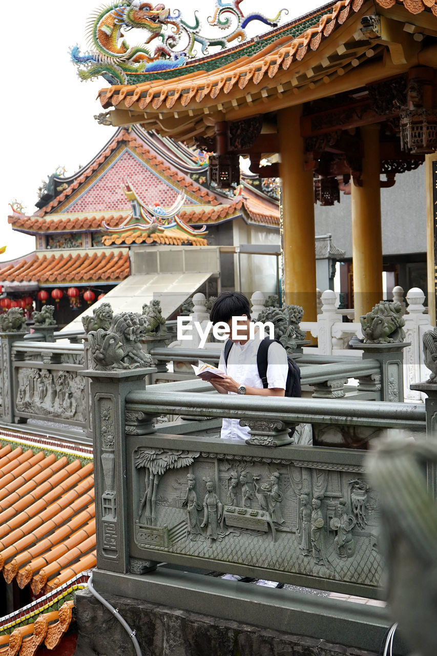 Man reading book while standing by railing in temple
