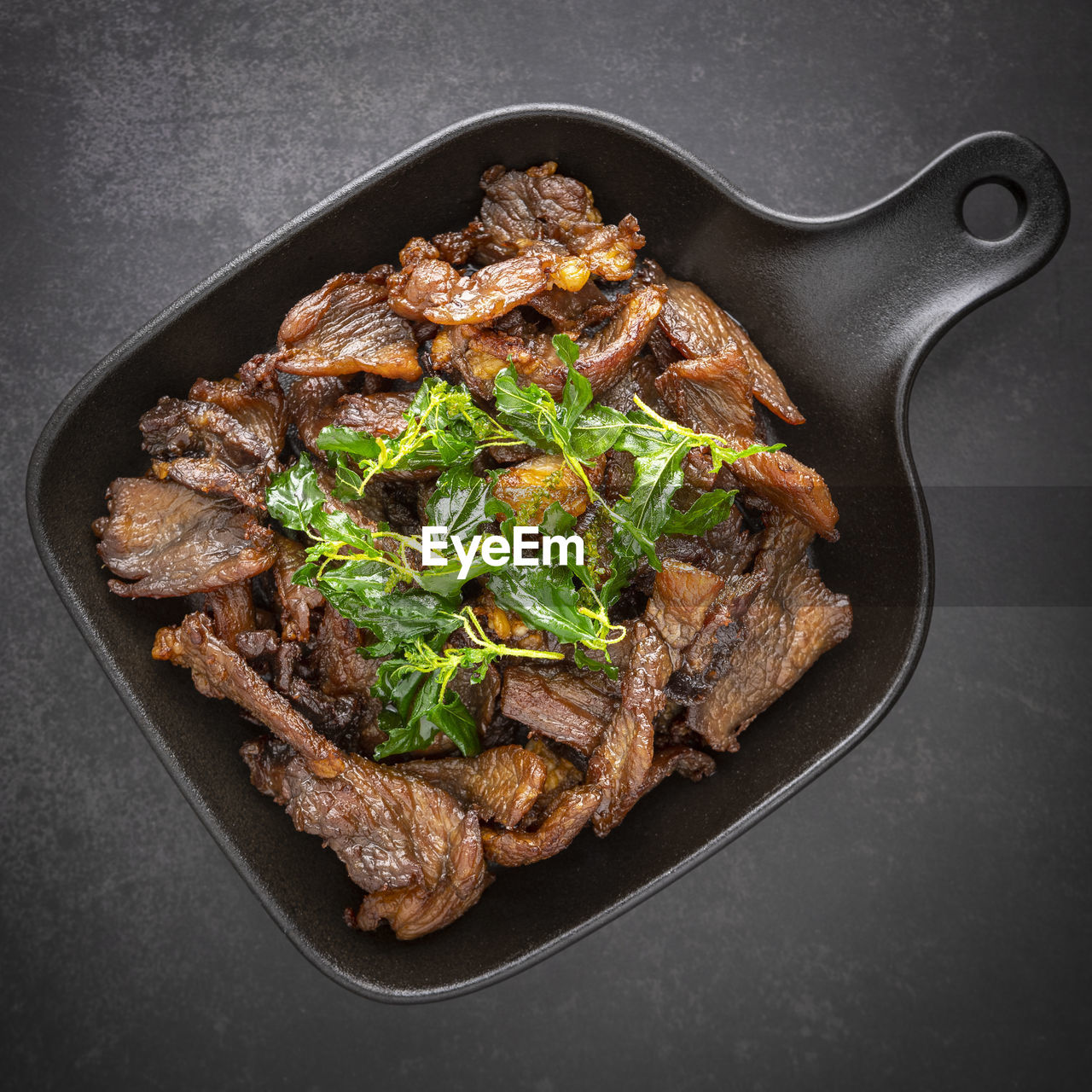 Thai food, fried sun dried beef with crispy basil leaves in black pan on the dark tone background