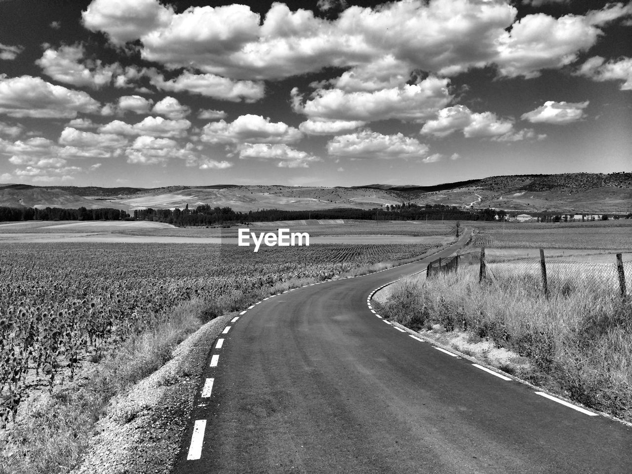 Road passing through field against cloudy sky