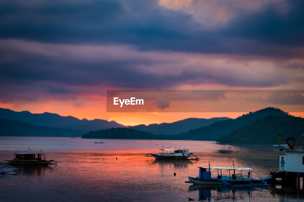 Sailboats moored on sea against sky during sunset