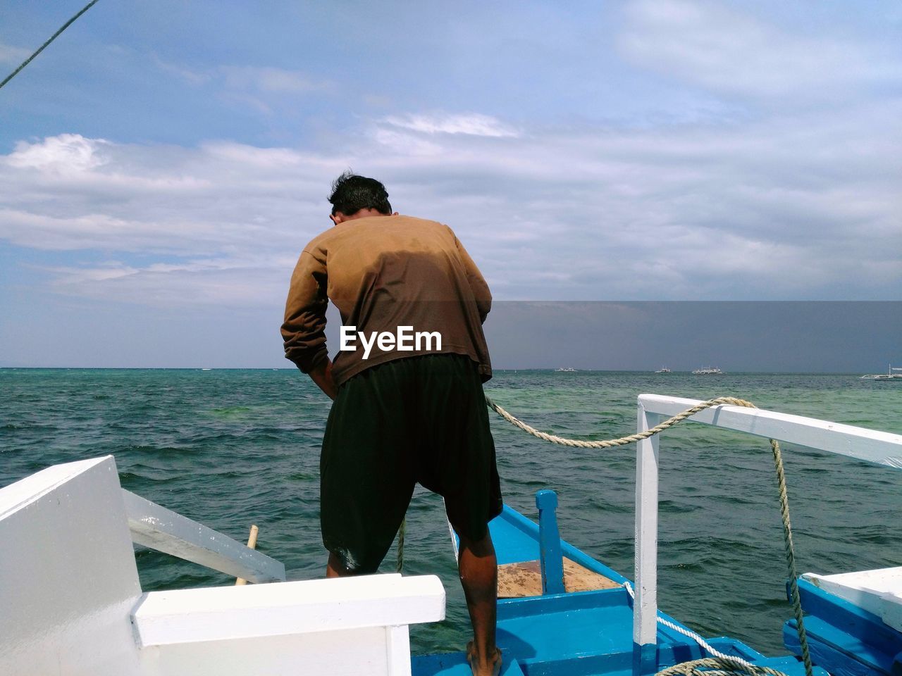 Rear view of man standing in boat on sea against sky