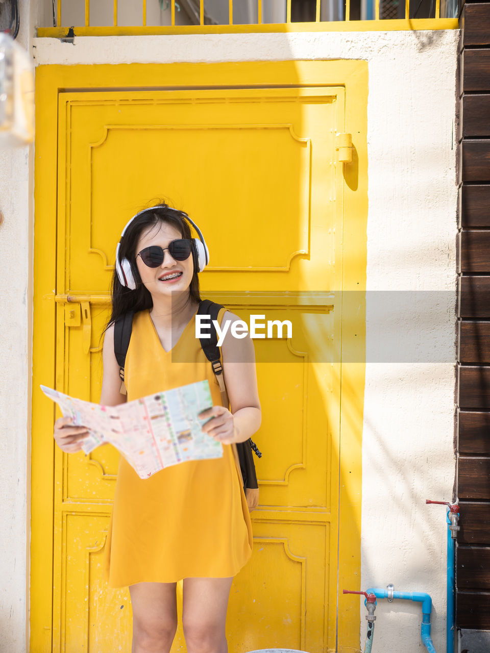 Smiling young woman holding map while standing against yellow door