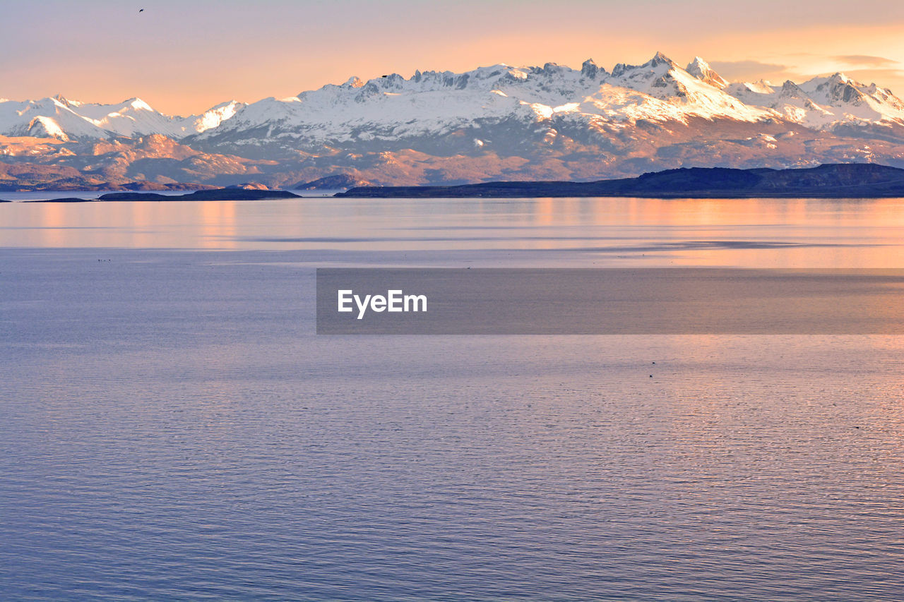 Scenic view of sea by snowcapped mountains against sky during sunset