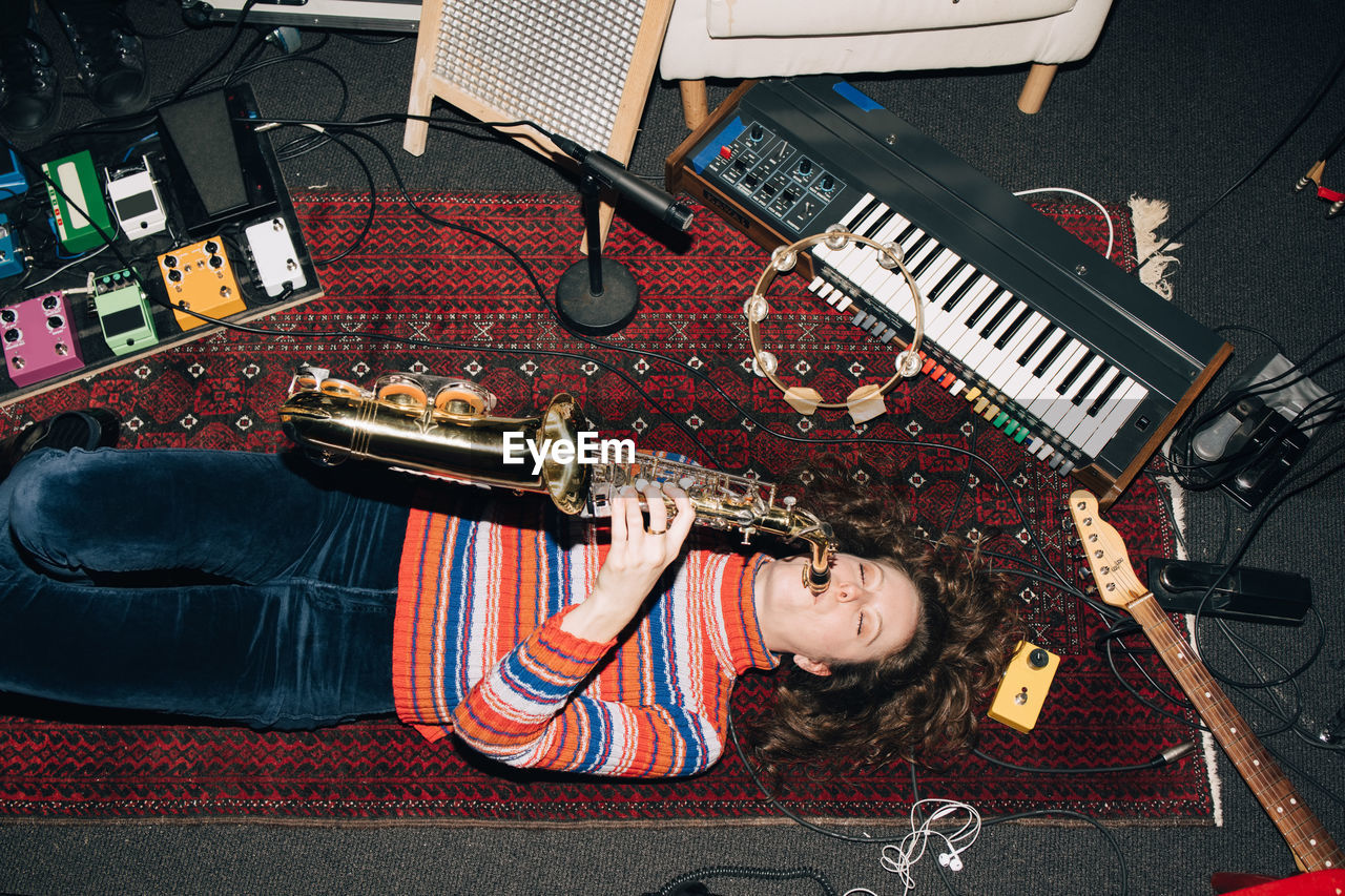 High angle view of smiling woman playing saxophone while lying on carpet at studio