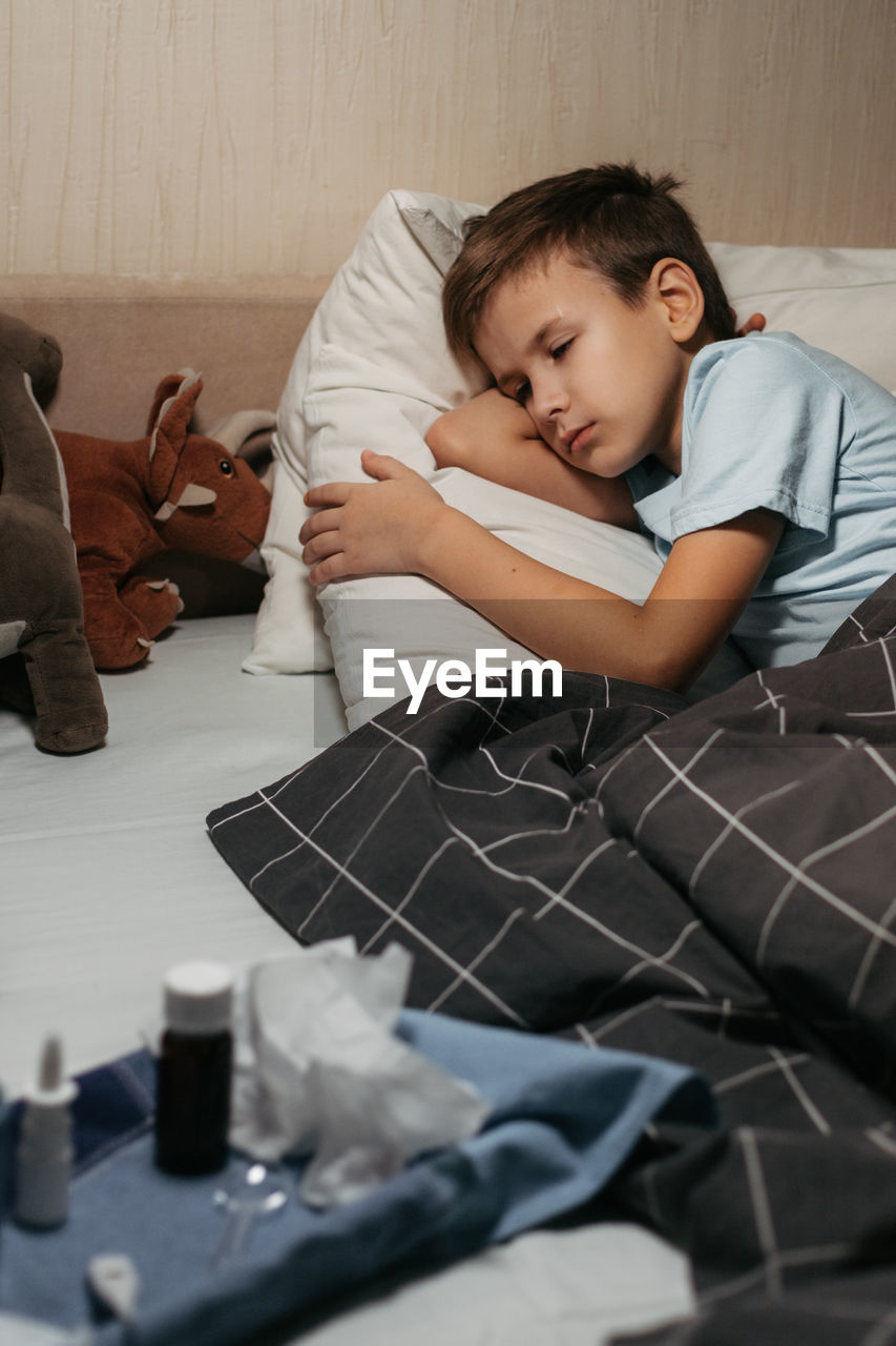 Tired ill child laying in bed with close eyes. some medicines are nearby